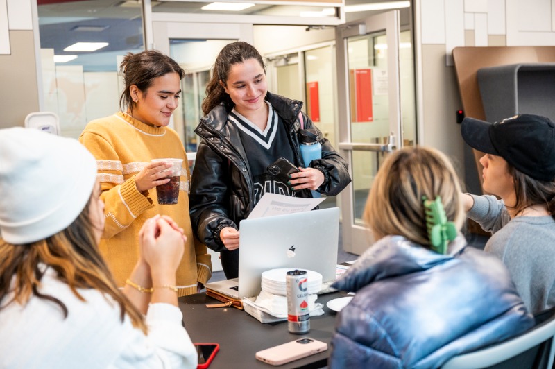 Two students check in at a table for an event. One student checking in has a piece of paper.
