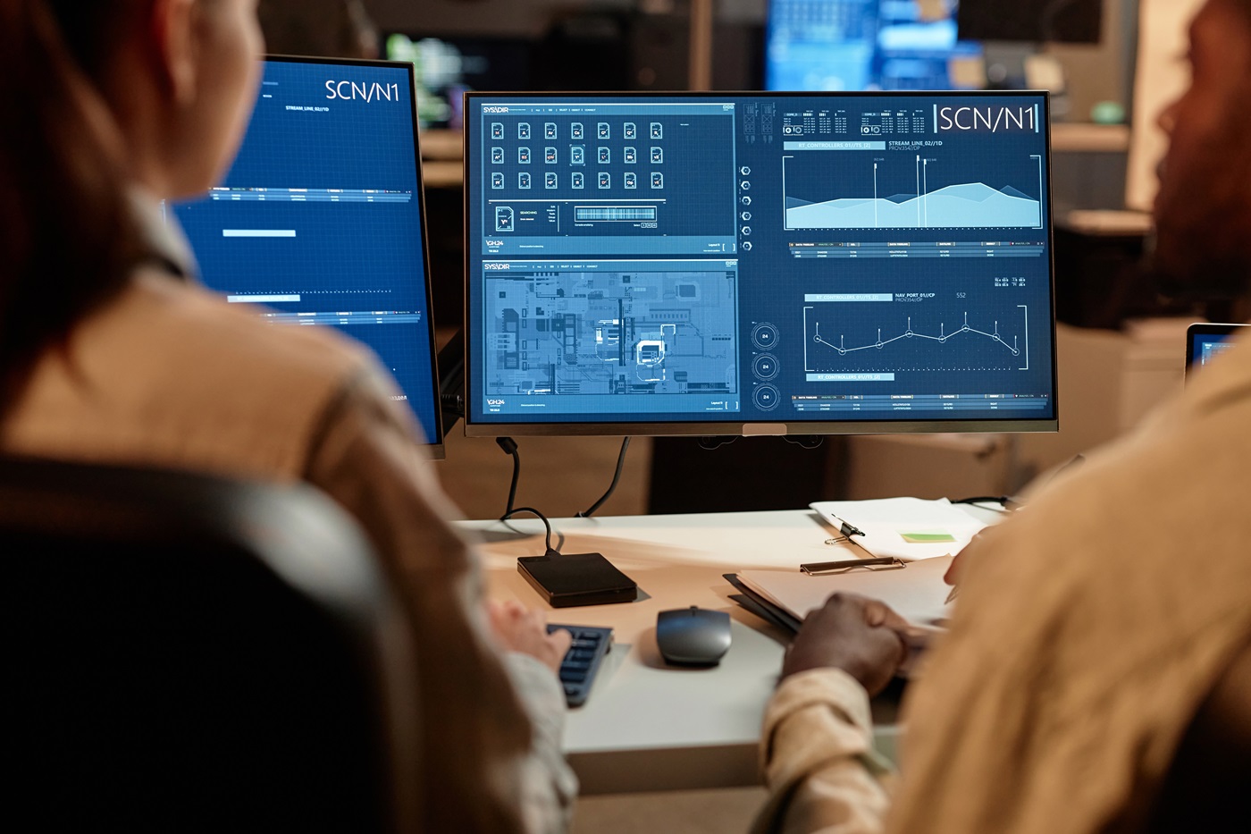 Two people analyzing data on multiple computer monitors.