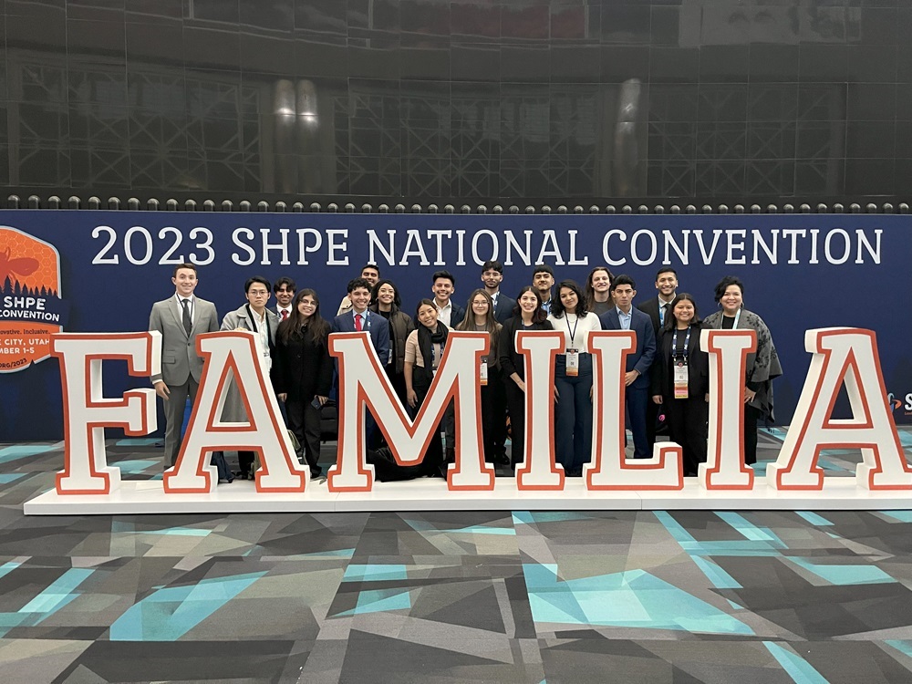 A group of diverse students smiles behind a large "FAMILIA" sign at the 2023 SHPE National Convention.
