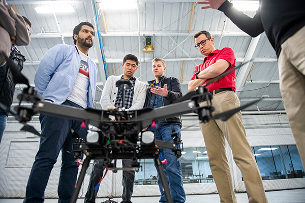 Students and a faculty member examine a large drone during a research session in a university lab setting.