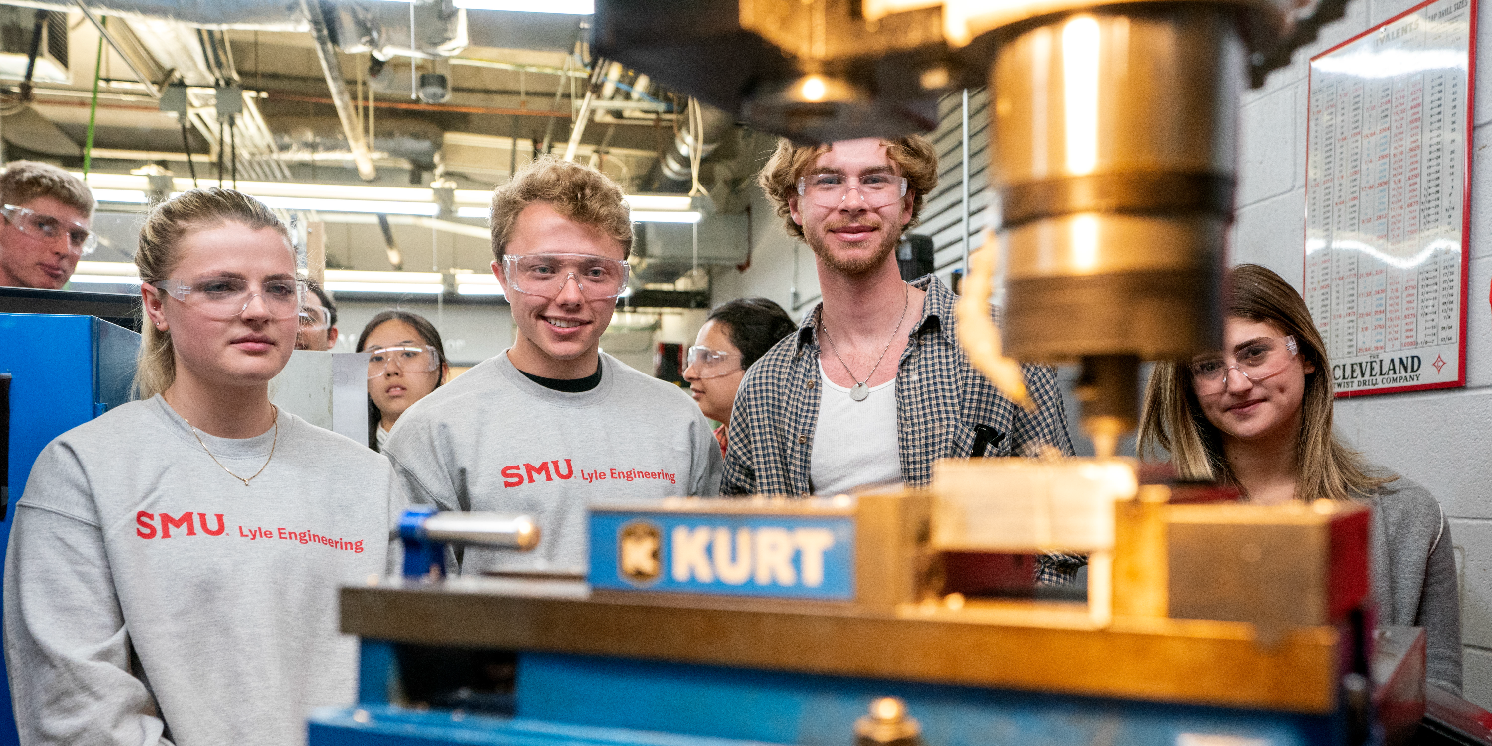 Student wearing an 色花堂_色花堂 98堂 Lyle Engineering sweatshirt smiling and holding up a metal manufacturing part.