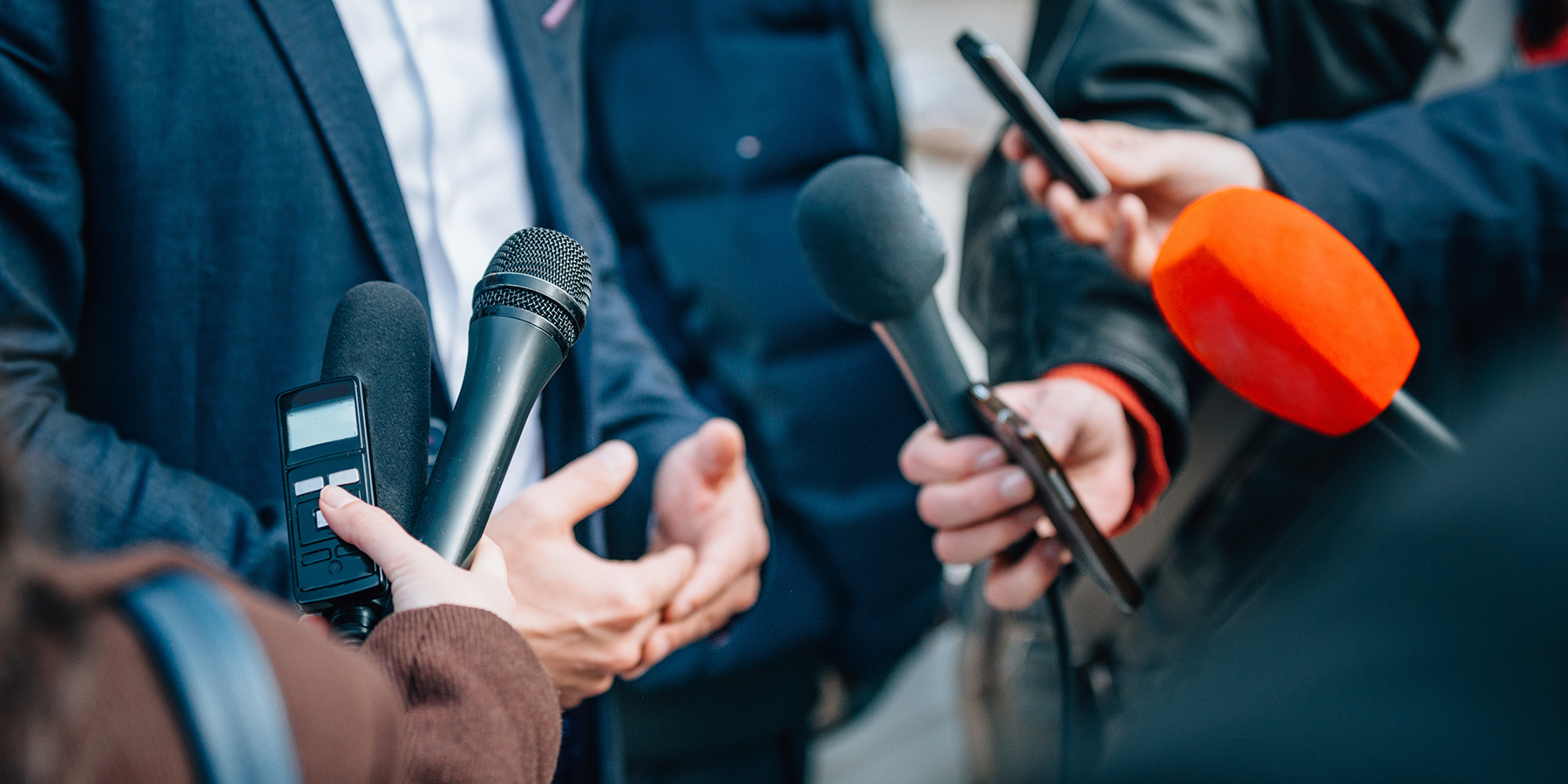Close up of a person in a suit being interviewed by multiple journalists at a press conference