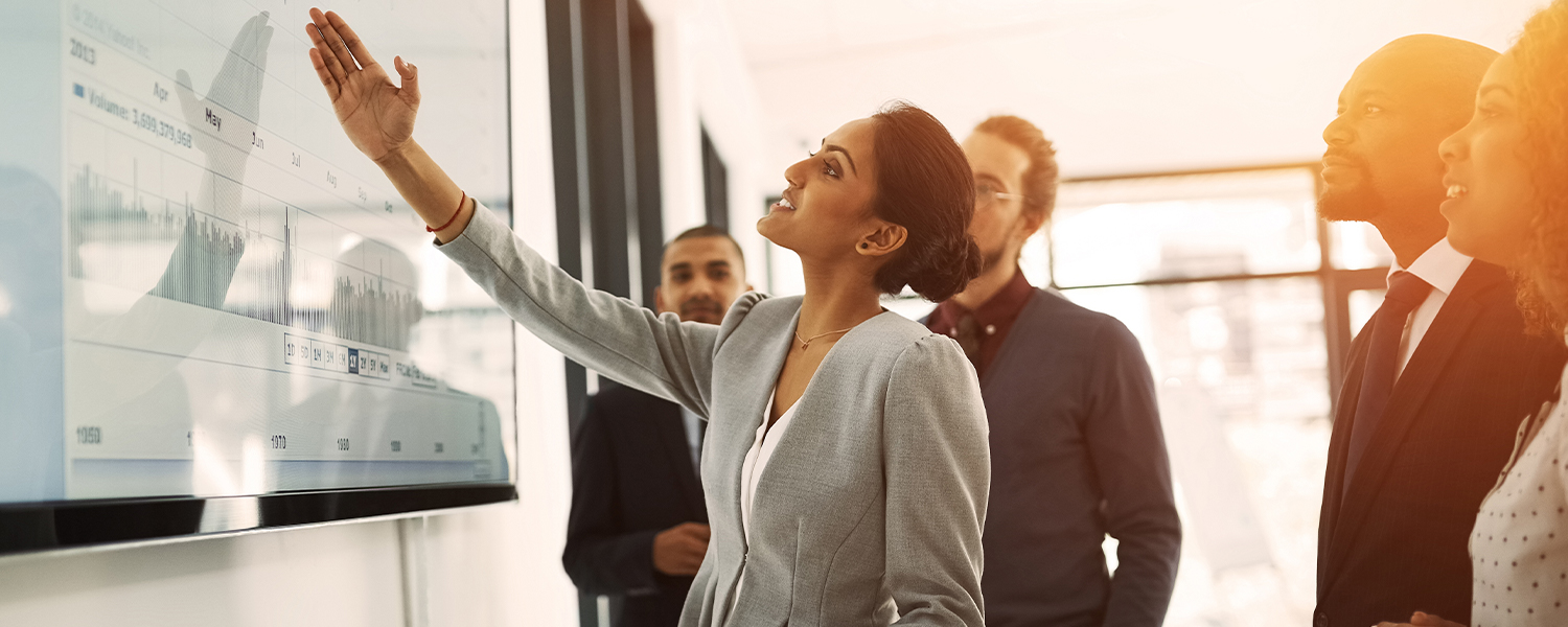 A woman leading a business presentation, pointing to a screen in front of her colleagues