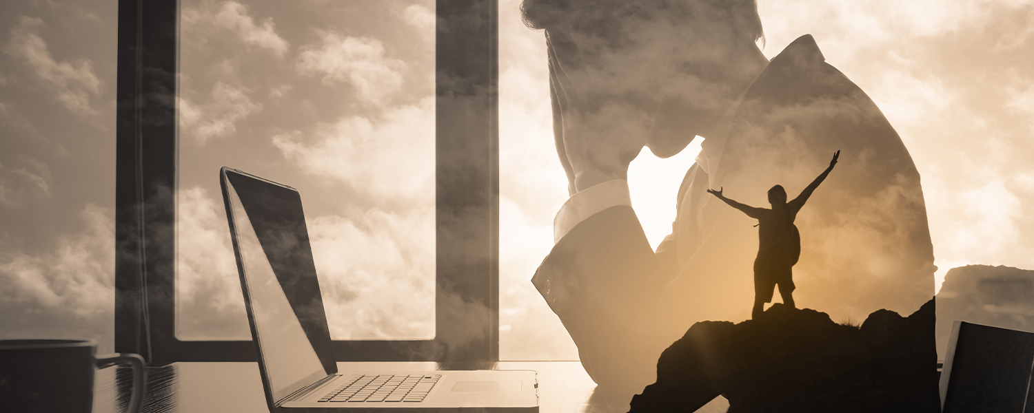 A silhouette of a businessman slumped in front of a computer. Inside the silhouette is a hiker on top of a cliff, celebrating success.