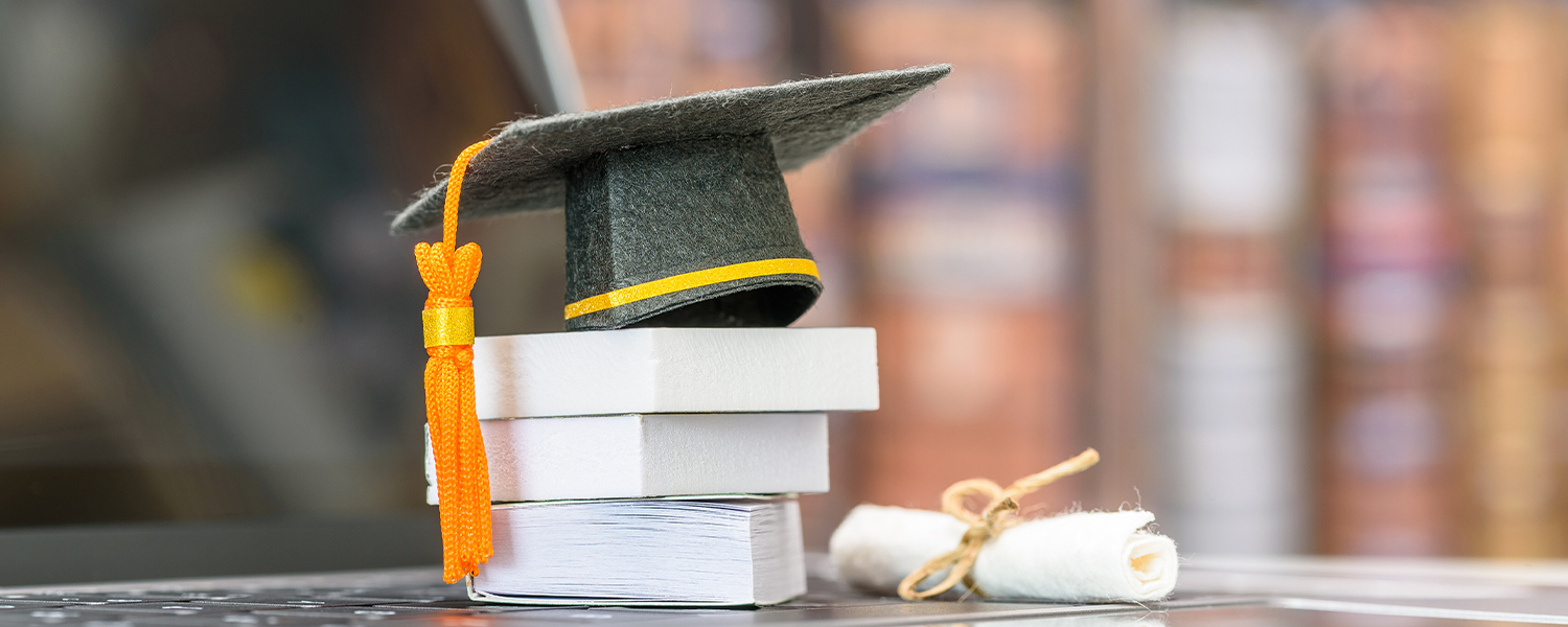 A photo of tiny little bits of paper, stacked as if they were books, along with a tiny diploma and a miniature graduation cap.
