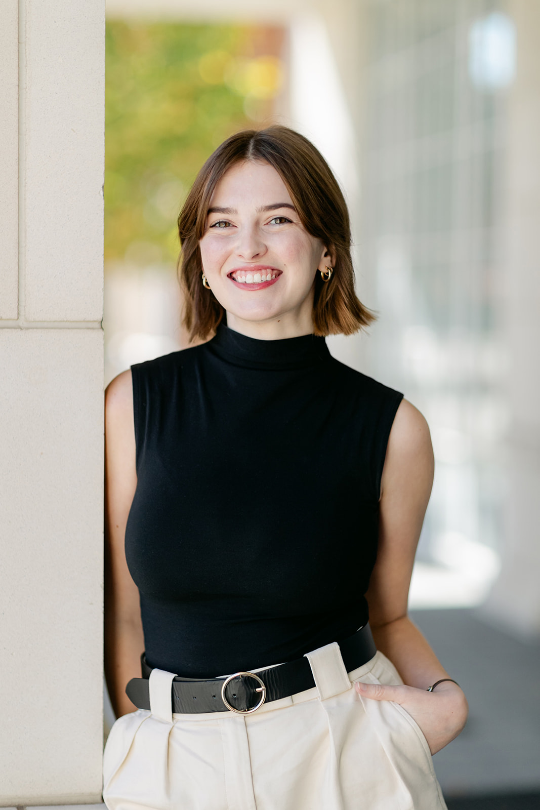 smiling woman in black top and tan slacks leaning against a column