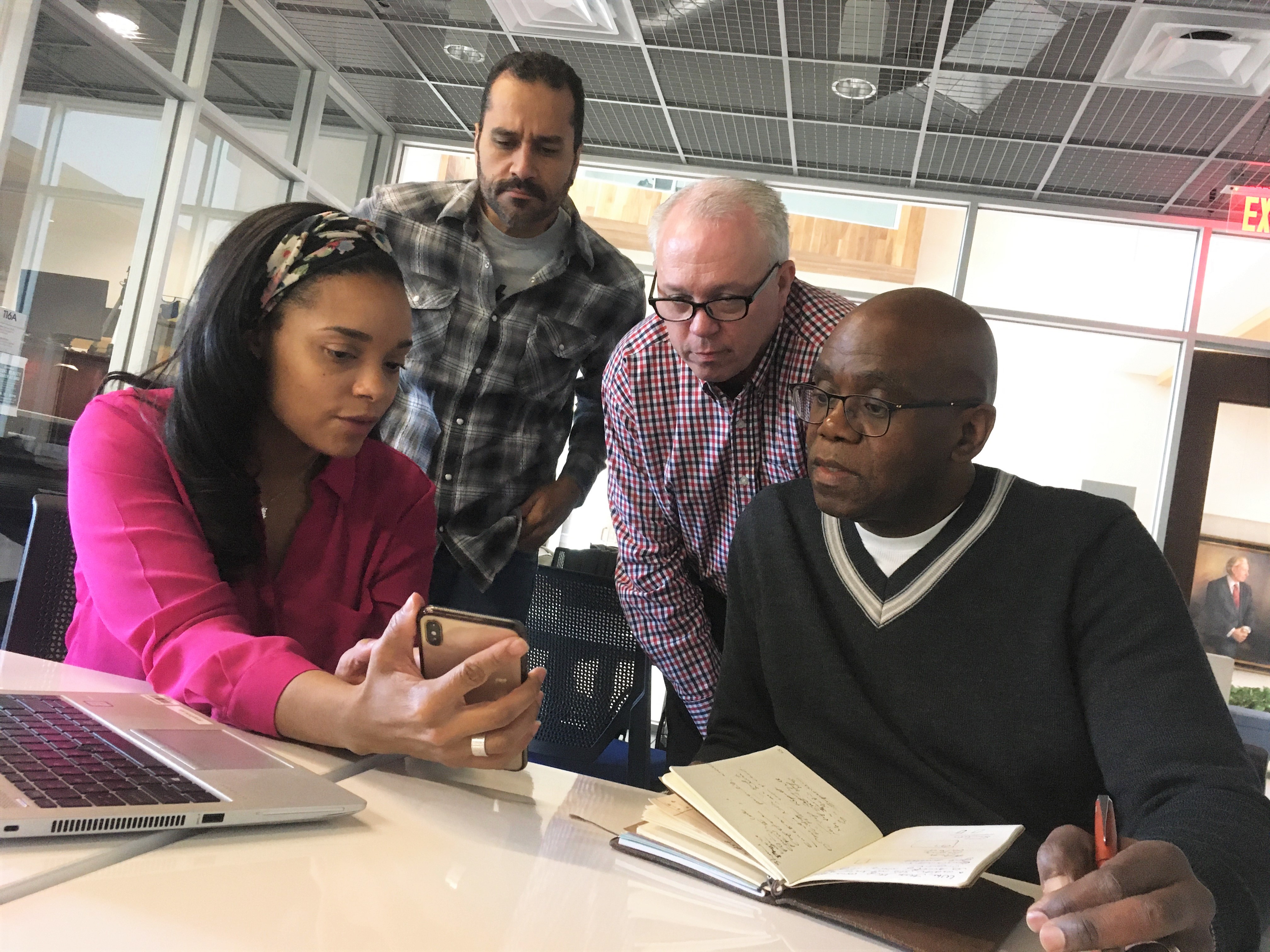 Four people sharing information at a table with phones, laptop, notebook