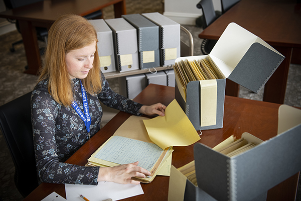 woman sits at desk with archival boxes surrounding her and reads through letters.
