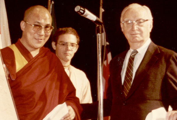 Dalai Lama stands next to a microphones with Outler and another man