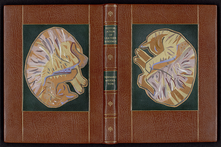 Cover of a brown book with cats curled up sleeping on the front and back. Gold writing on the spine "Restoration of Leather Binding Bernard Middleton".
