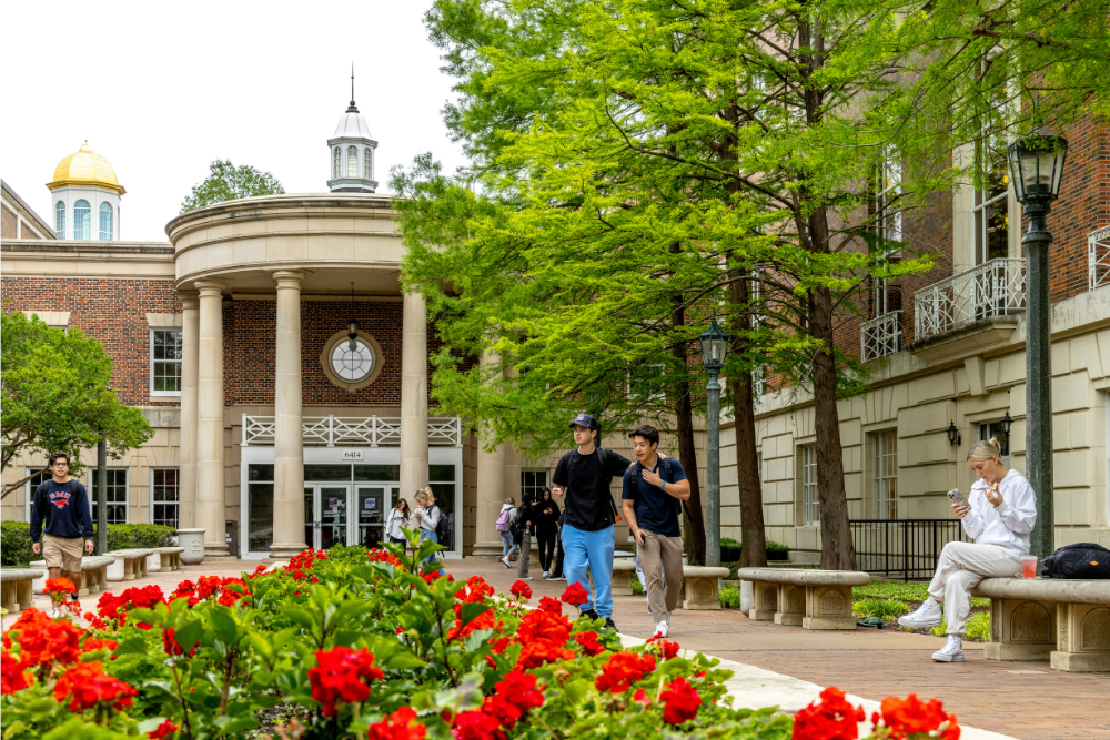 The front of the Fondren Library building with red flowers in the foreground