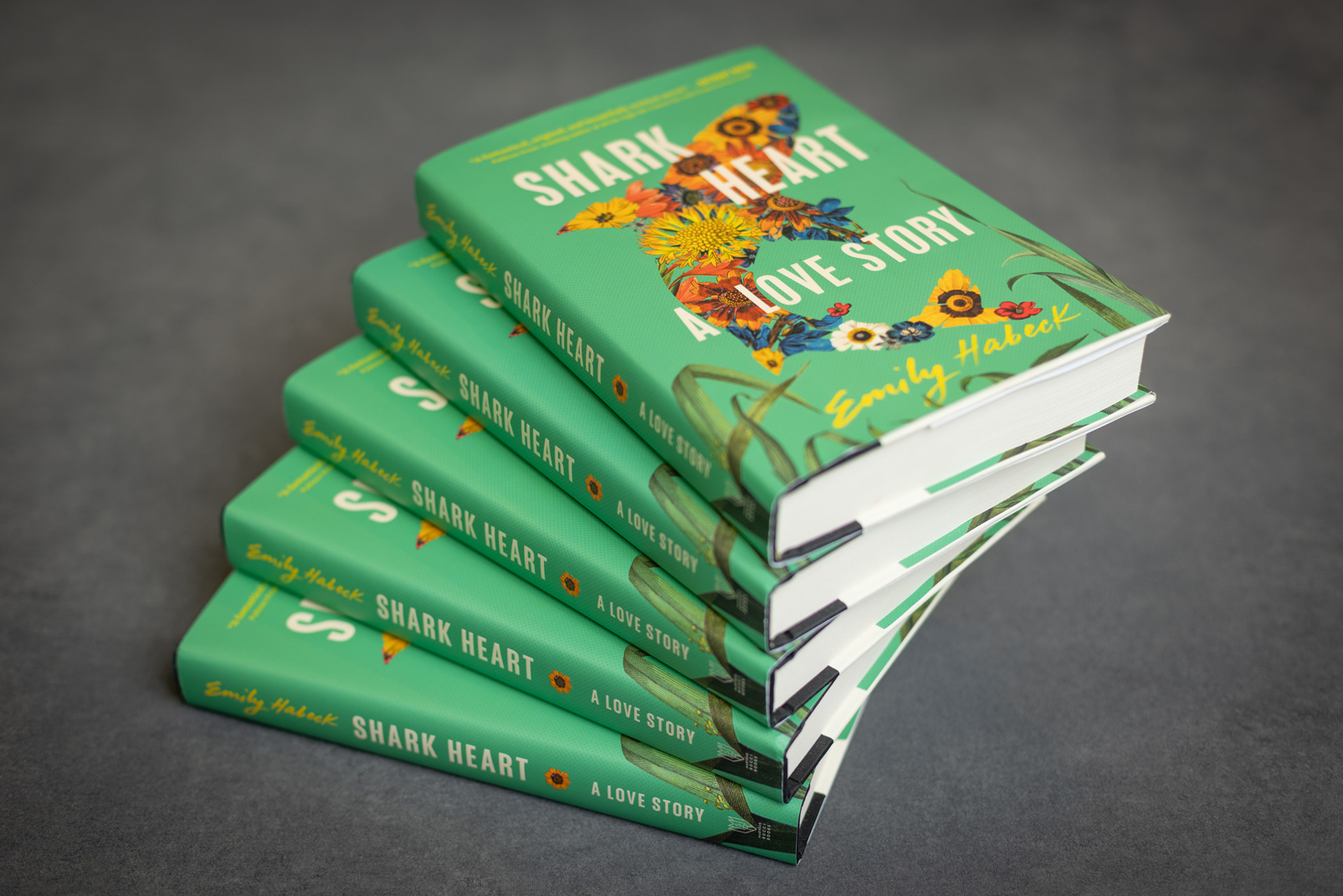 Pile of green books titled Shark Heart by alum and author Emily Habeck