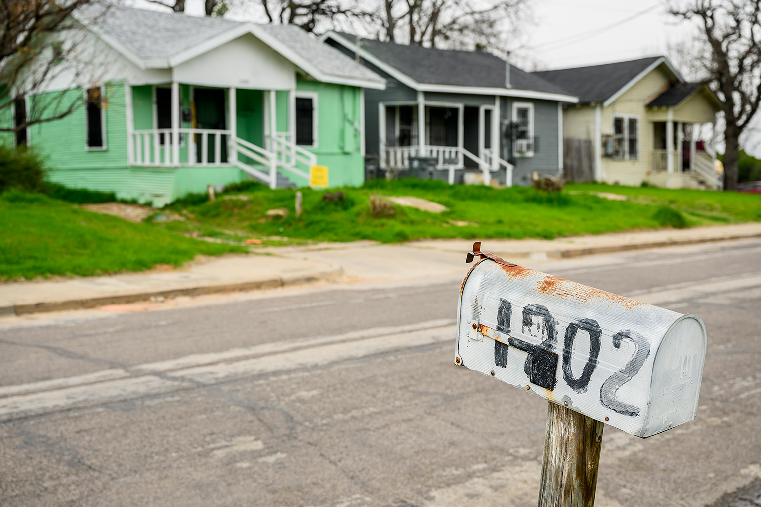 A worn mailbox is shown in front of a light-green colored home