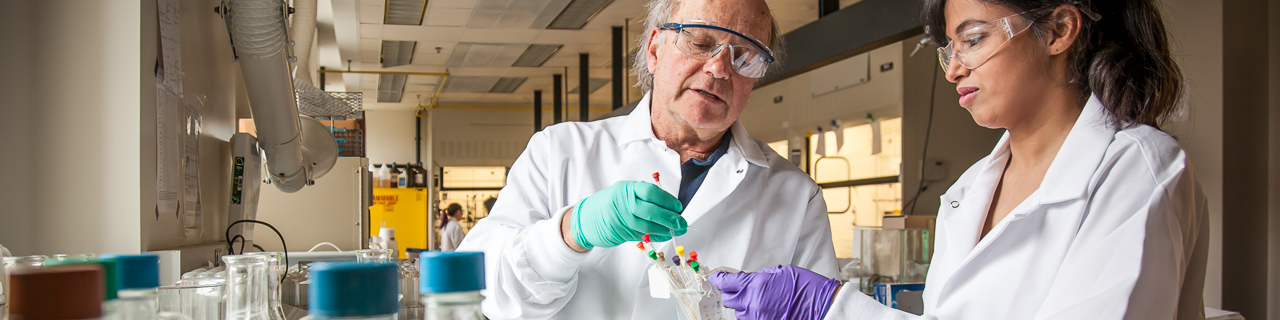 Dr. John Buynak demonstrating chemistry research technique with a student