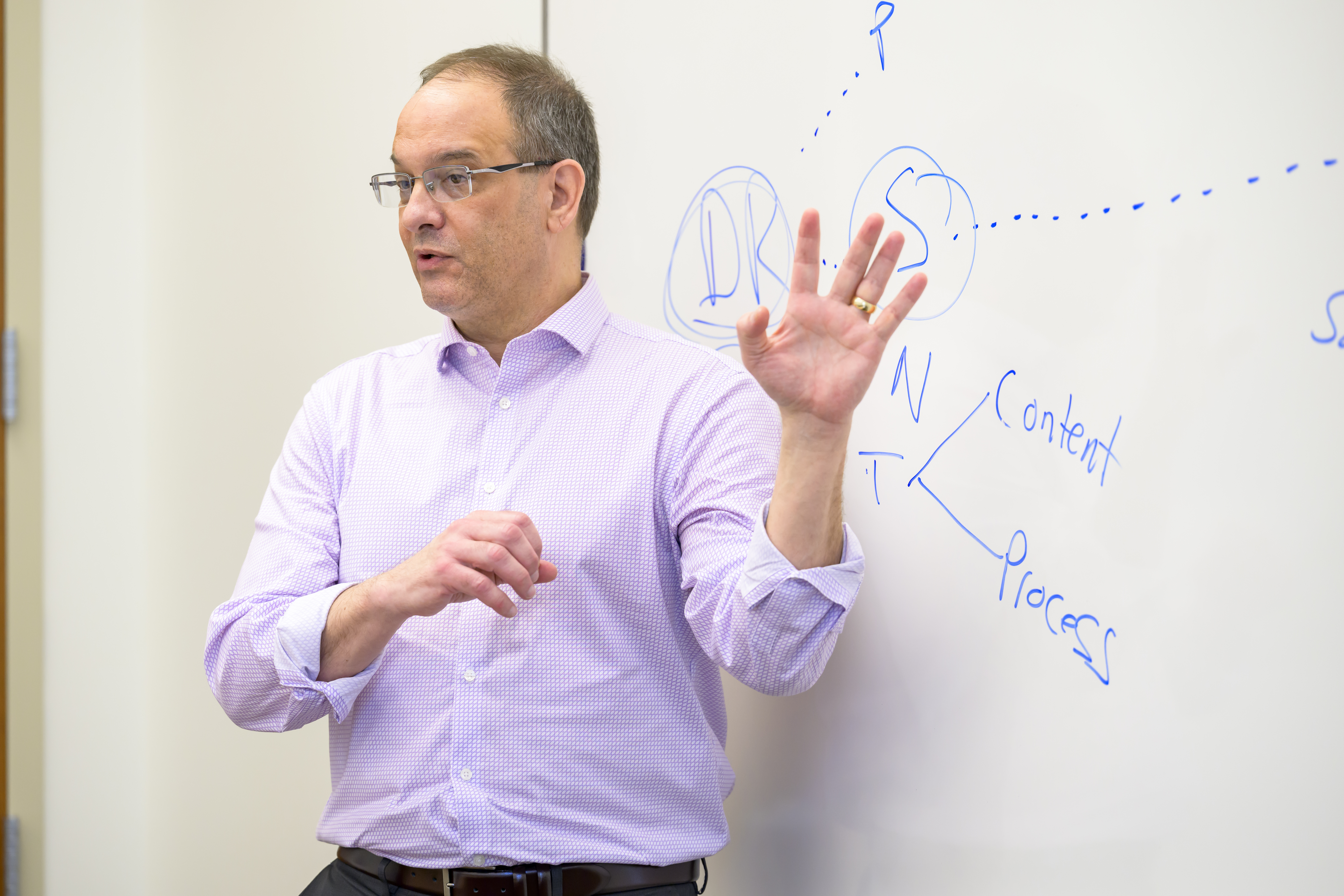 A professor lectures in front of a white board with a map on it