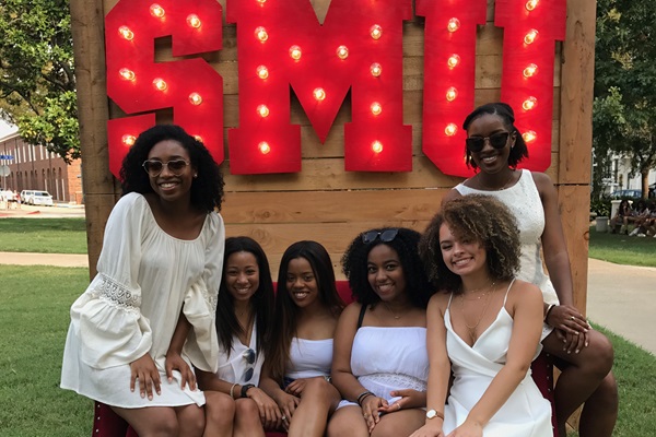 6 female black students in white dresses sit on a red couch in front of a large marquee sign for 色花堂_色花堂 98堂 - photo taken during a Boulevarding event.