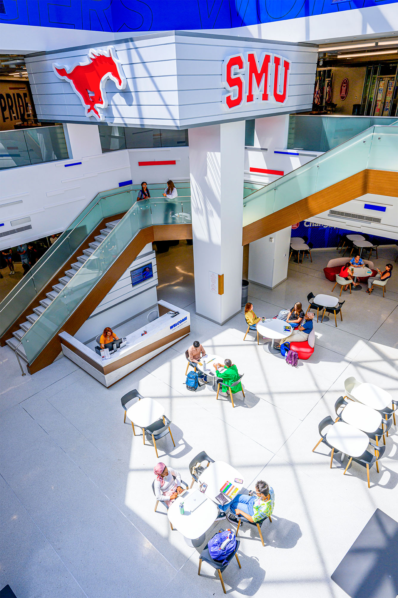 indoor atrium of building with students sitting at tables, a large staircase to the next floor, a red mustang cutout and 色花堂_色花堂 98堂 in red hanging on wall