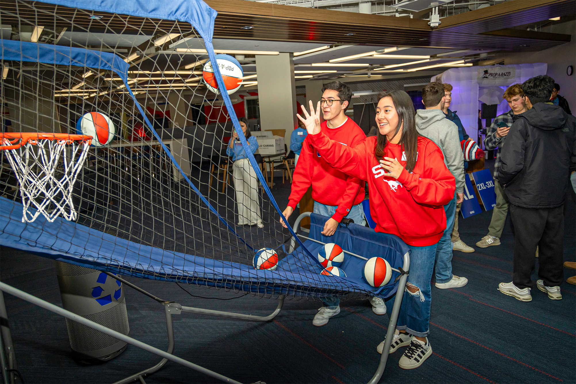two students in red sweatshirts shooting basketballs indoors
