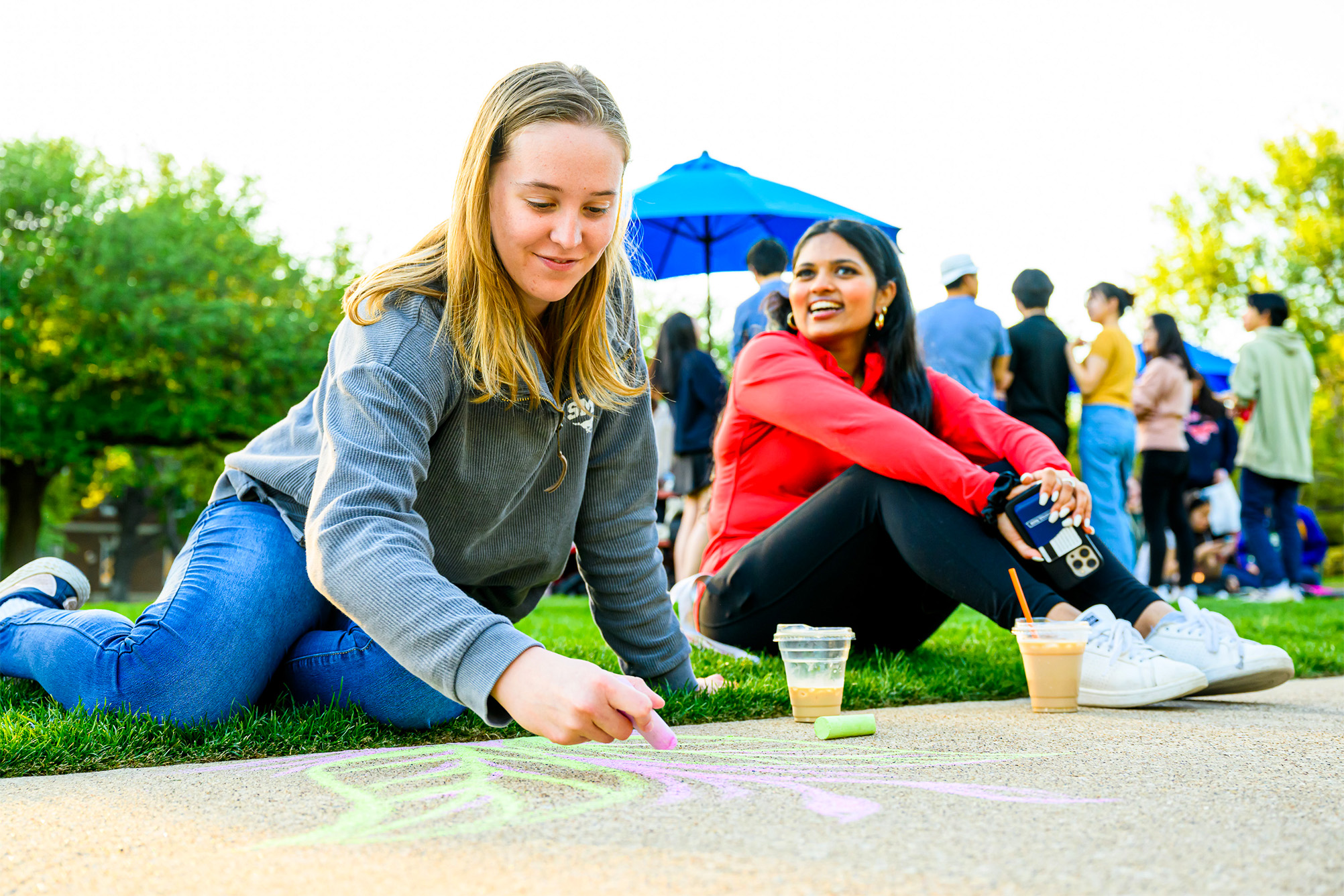 two students sitting outside on sidewalk with chalk