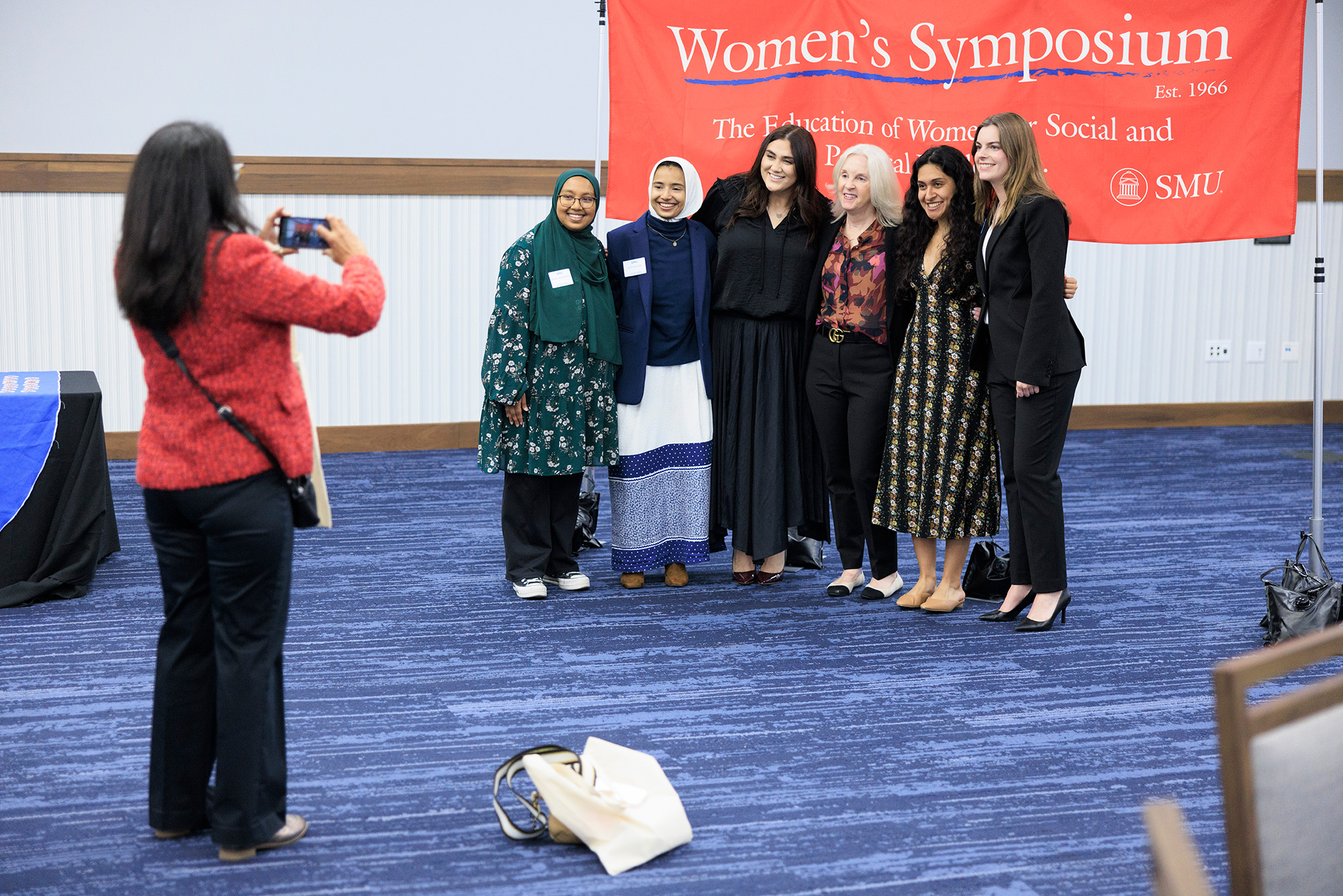 group of people standing indoor in front of red banner taking a photo